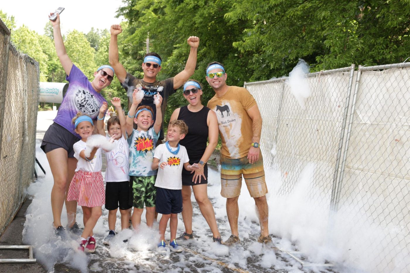 Two families with arms raised in celebration, covered in mud and foam at the end of an obstacle course.
