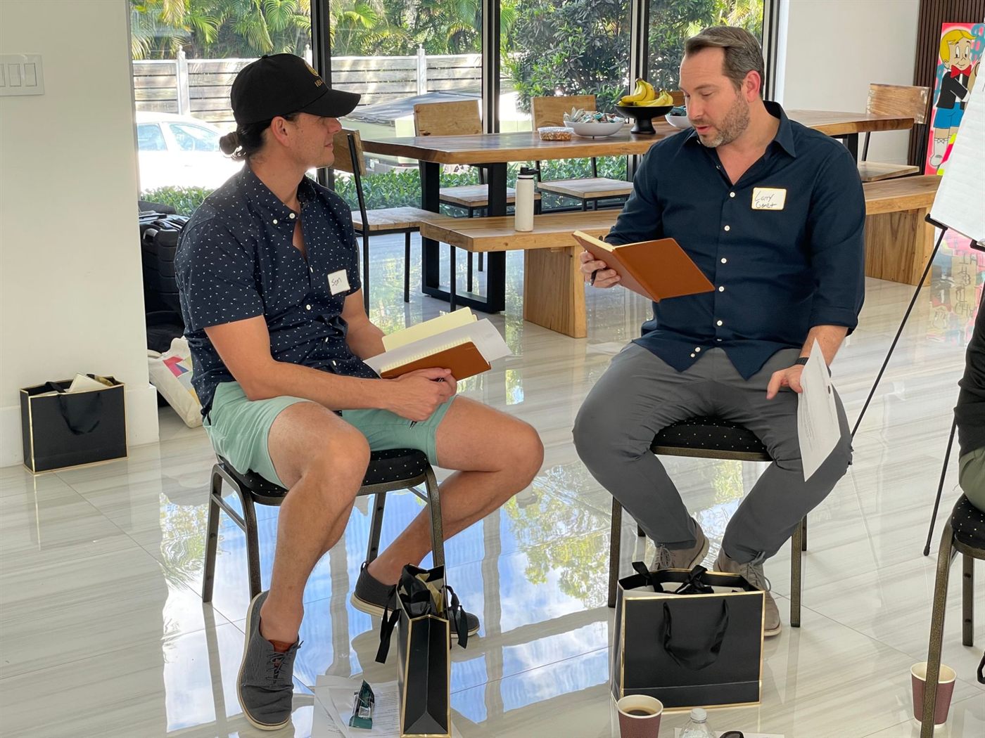 Two members seated on stools facing each other with notebooks and name tags during a workshop session.