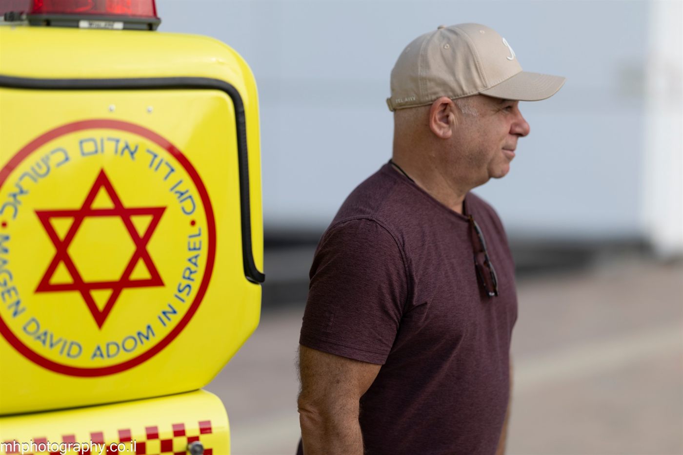 A member in a cap standing beside a yellow Magen David Adom ambulance marked with a red Star of David.