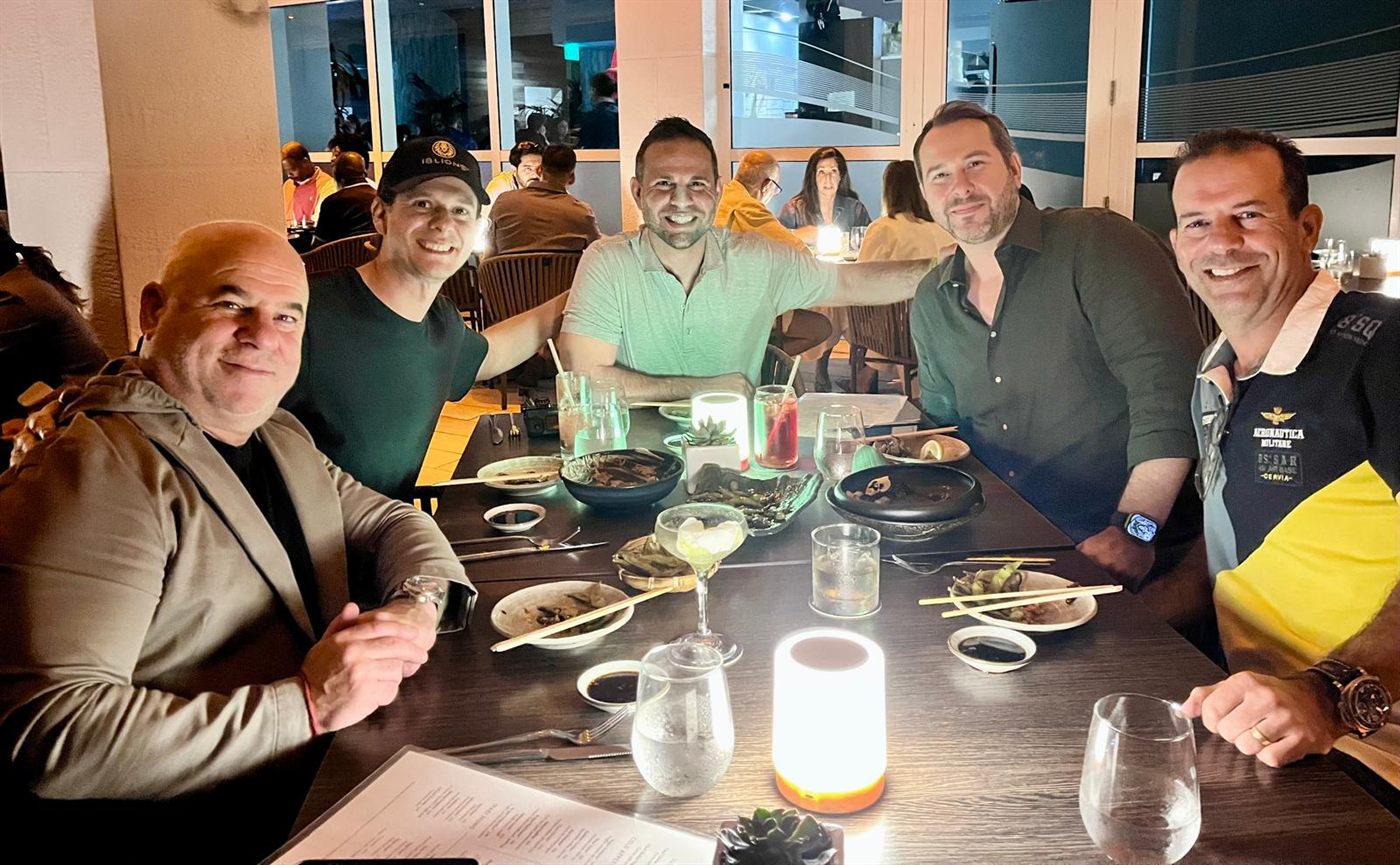 Five members seated around a restaurant table mid-meal, leaning in toward the camera.