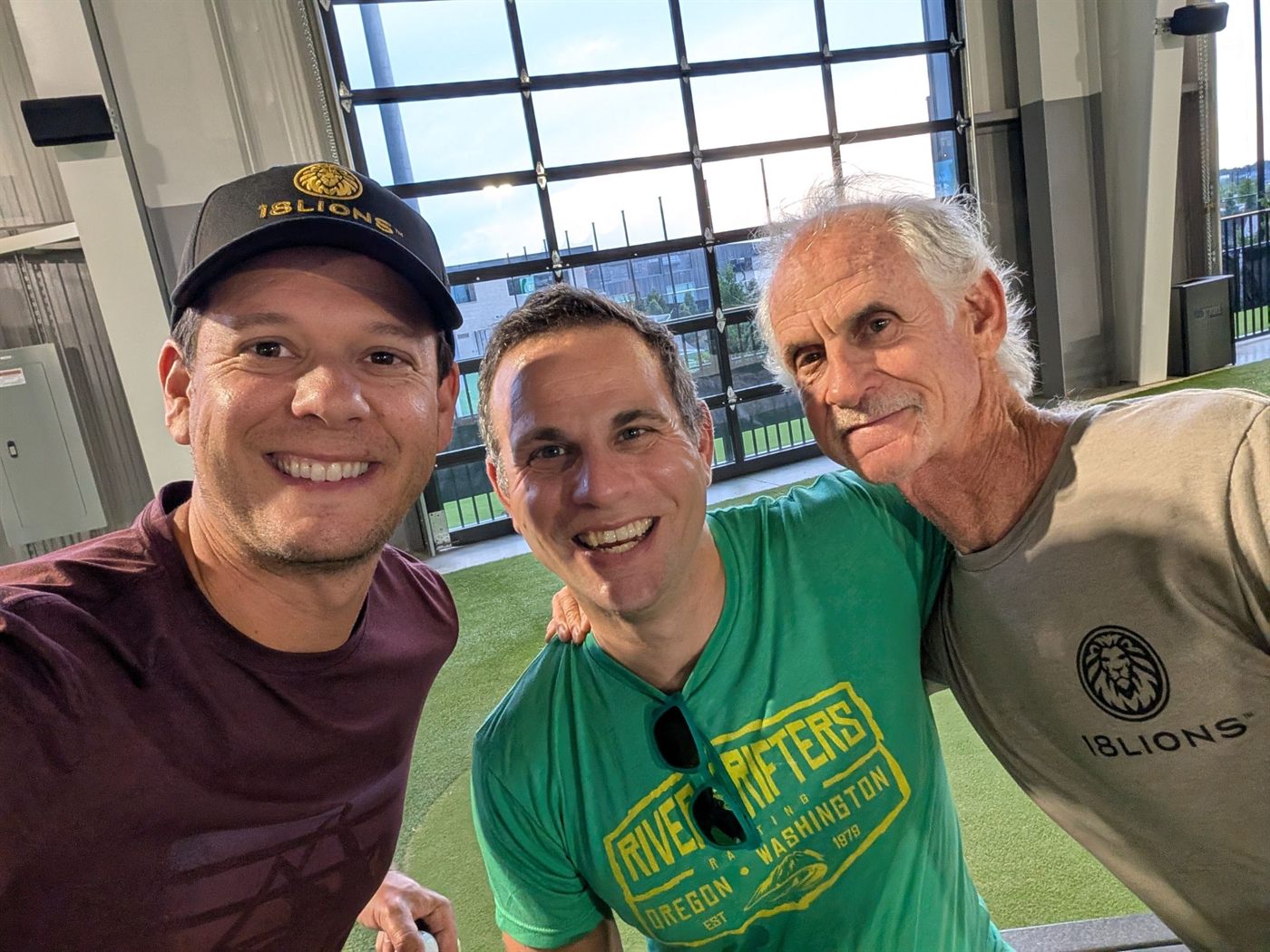 Three members posing for a selfie at a driving range, two wearing 18Lions apparel.